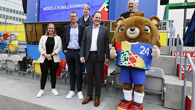 Menschen stehen mit dem UEFA EURO Maskottchen zusammen