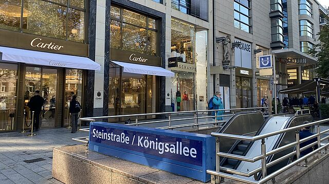 Königallee mit U-Bahnstation Steinstraße/Königsallee im Vordergrund und Geschäften im Hintergrund.