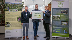 Drei Männer halten die Auszeichung hoch