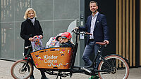 Personen stehen neben einem Lastenfahrrad, zwei Kinder sitzen drin