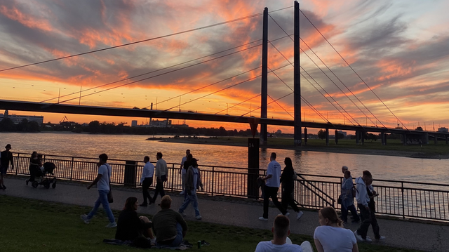 Menschen am Rhein mit rotgoldenem Himmel im Hintergrund