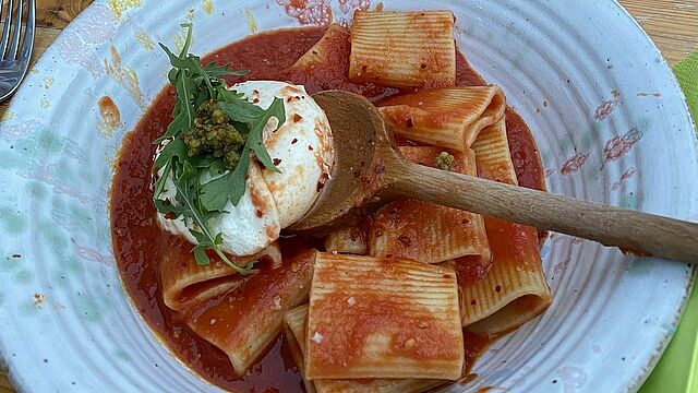 Ein Teller mit Nudeln und Tomatensoße und Burrata auf einem Holzlöffel.