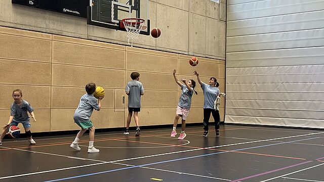 Kinder werfen Bälle auf einen Korb