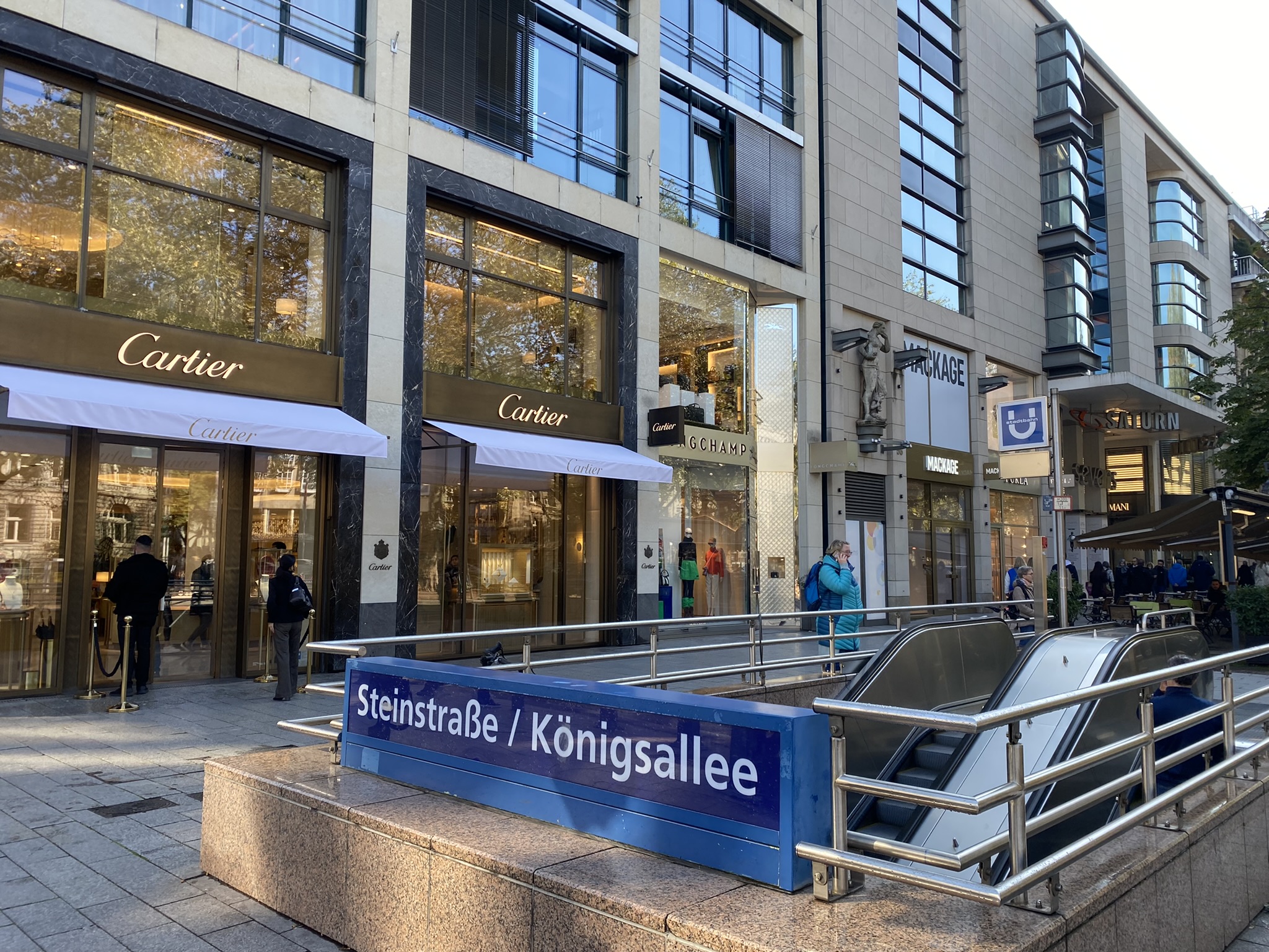 Königallee mit U-Bahnstation Steinstraße/Königsallee im Vordergrund und Geschäften im Hintergrund.